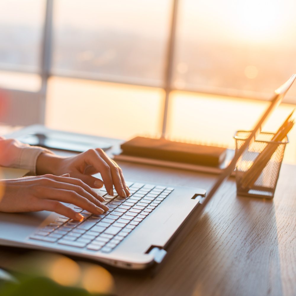 Laptop on desk with sun setting in background.