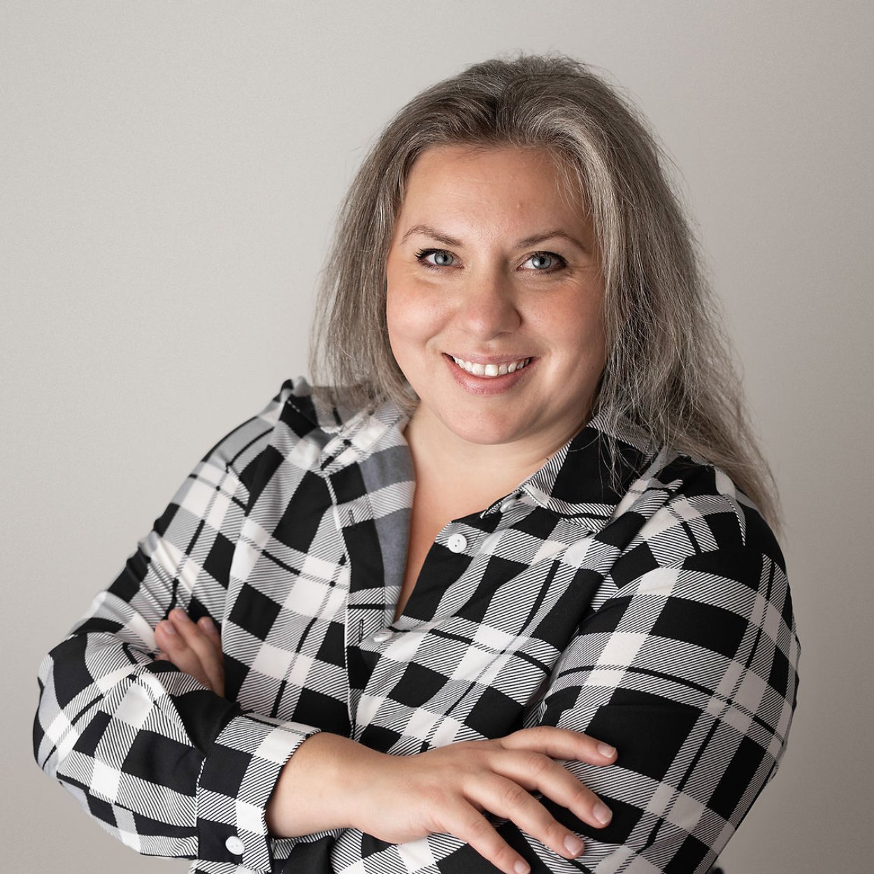 Headshot of woman in plaid shot, arms crossed in a black plaid shirt.