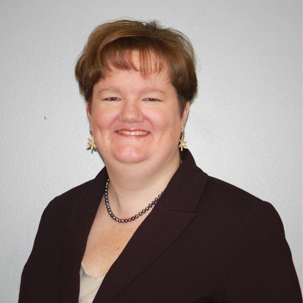 Headshot of woman with short red hair in a brown blazer with a friendly smile.